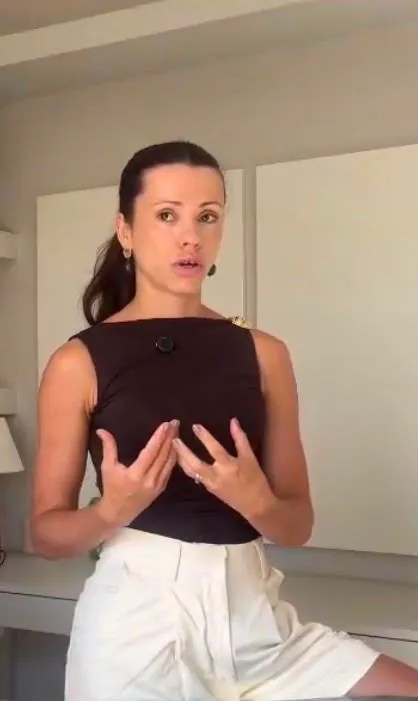 Raíza gesticulando com as mãos enquanto fala, vestindo blusa preta, em aula da coluna.